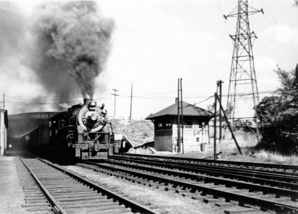 A locomotive heads south out of Concord under a full head of steam past the train tower under the Route 3 bridge.