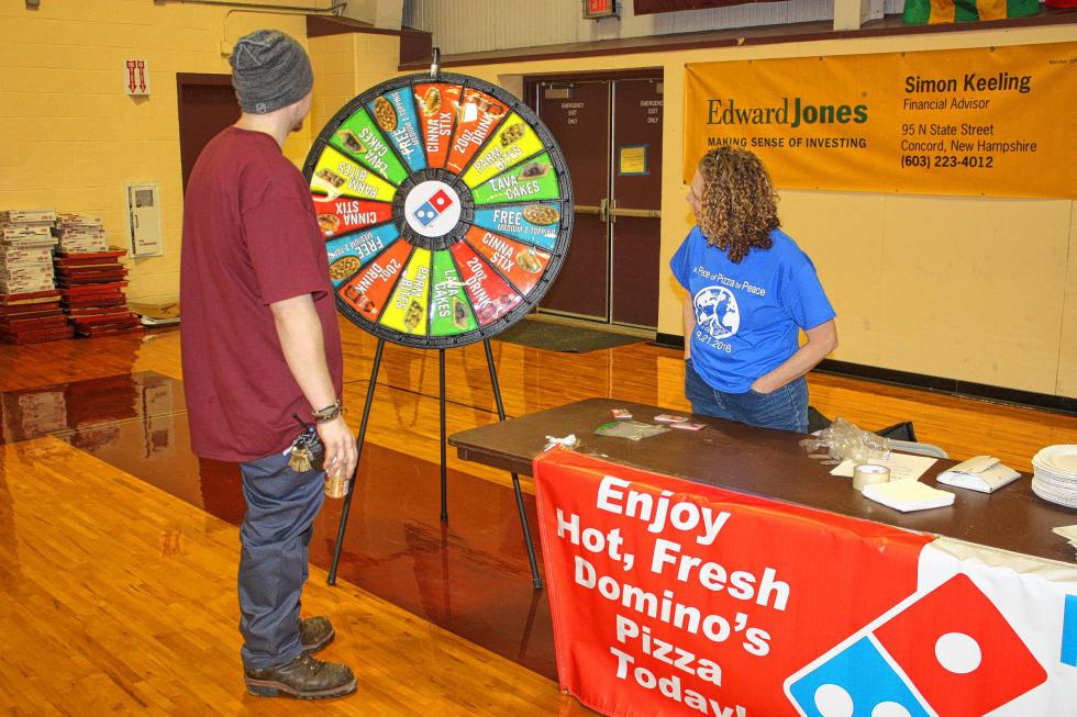 Josh Douillette, a maintenance worker at NHTI, spins the prize wheel at the Domino's station at NHTI's Pizza Wars last week. Dawn Ruddy with Domnio's watches anxiously.  (JON BODELL / Insider staff) -