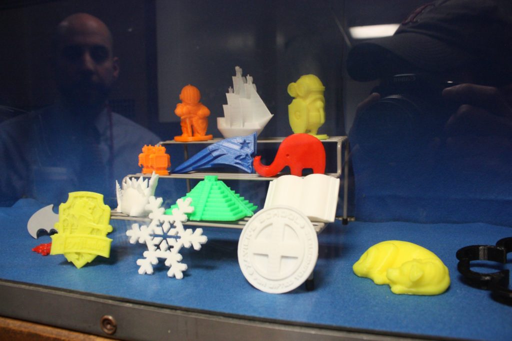 Although Concord Public Library’s 3-D printer (left) is just going live to the public today (March 7), the staff has already created a bunch of little figures (right) to get a feel for the machine. Some worked out fine while others failed – teaching the staff valuable lessons in the process. These figures – including a Patriots logo, an elephant and a sleeping dog – are on display at the library.