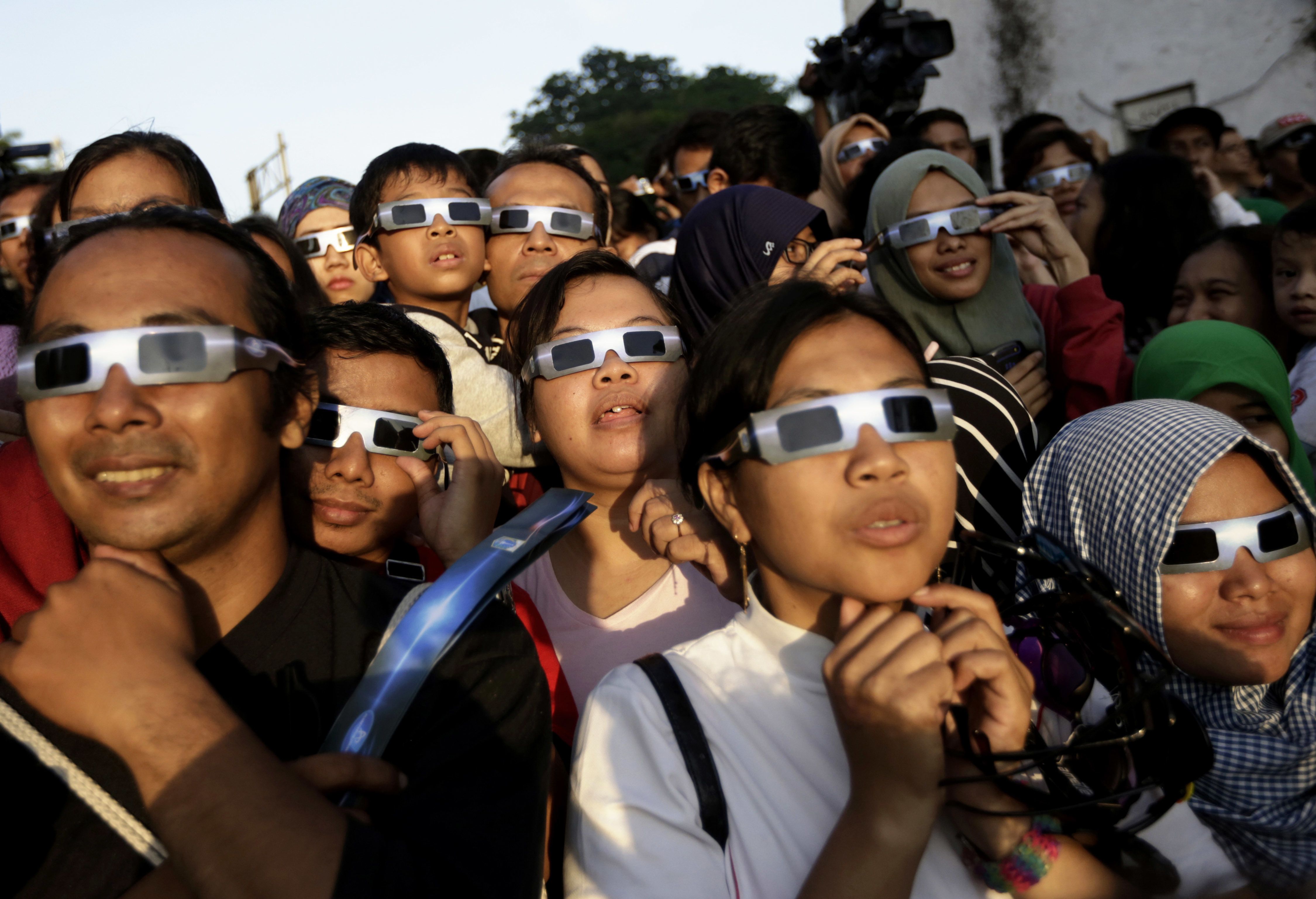 FILE - In this Wednesday, March 9, 2016 file photo, people wearing protective glasses look up at the sun to watch a solar eclipse in Jakarta, Indonesia. Doctors say not to look at the sun without eclipse glasses or other certified filters except during the two minutes or so when the moon completely blots out the sun, called totality. That’s the only time it’s safe to view the eclipse without protection. When totality is ending, then it’s time to put them back on.  (AP Photo/Dita Alangkara) Dita Alangkara