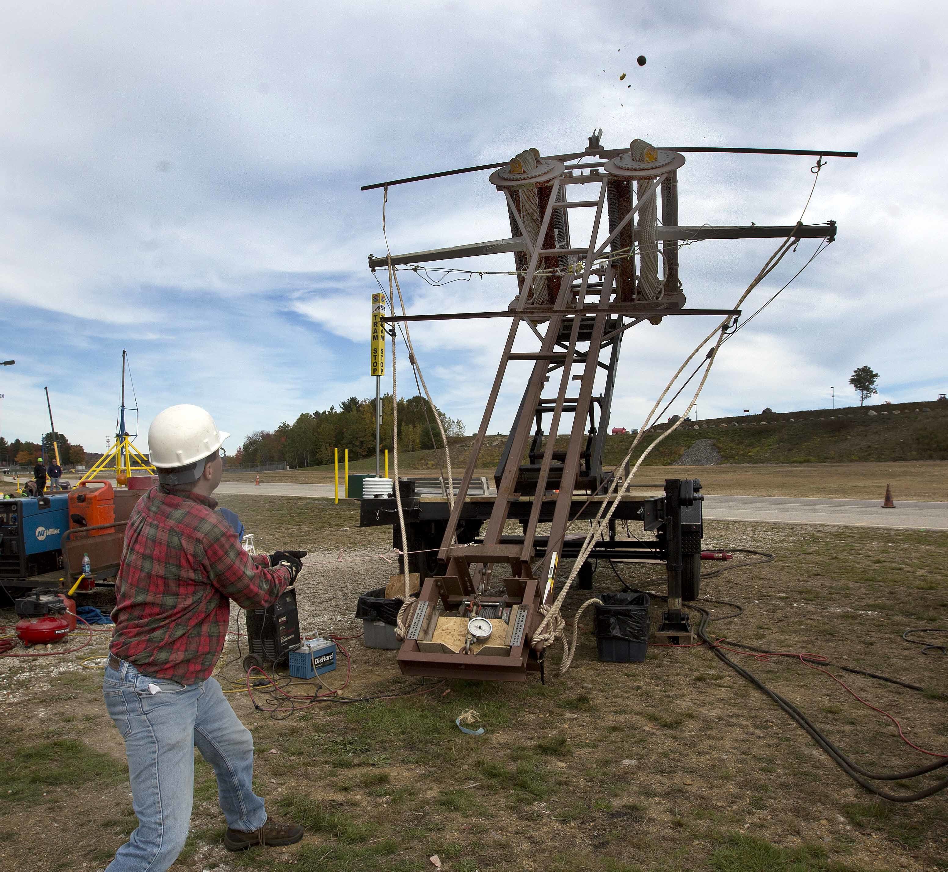 In this Saturday, Oct. 15, 2016 photo, Eric Ludlam, from Framingham, Mass. pulls the trigger on his pumpkin thrower "Mista Ballista" in Loudon, N.H. A design from a 400 BC rock thrower tosses a pumpkin more than 1,000 feet. Sixteen teams competed over the weekend at New Hampshire Motor Speedway for the longest pumpkin toss. (AP Photo/Jim Cole) Jim Cole