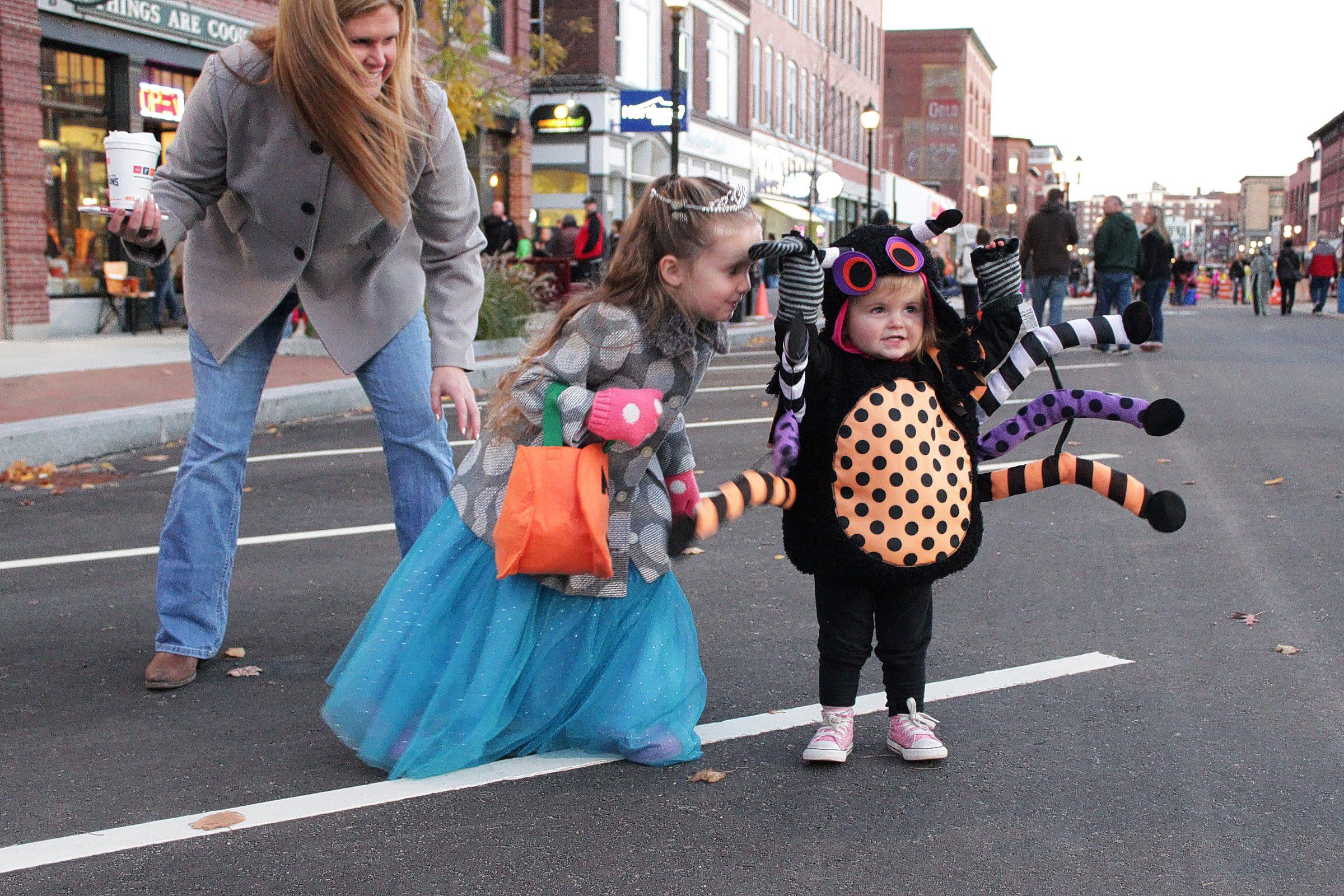 Paisley Callanan, 19 months, raises her arms to show off her spider costume with a little encouragement from her sister Lucy, 4, and her mom, Kelly, in downtown Concord on Friday, Oct. 30, 2015. The girls' father, Philip Callanan, is principal of Mill Brook School. Halloween Howl, an Intown Concord event, was held Friday. Children, pets and families in costumes trick or treated downtown, danced and participated in a costume parade.  (SUSAN DOUCET / Monitor staff) SUSAN DOUCET