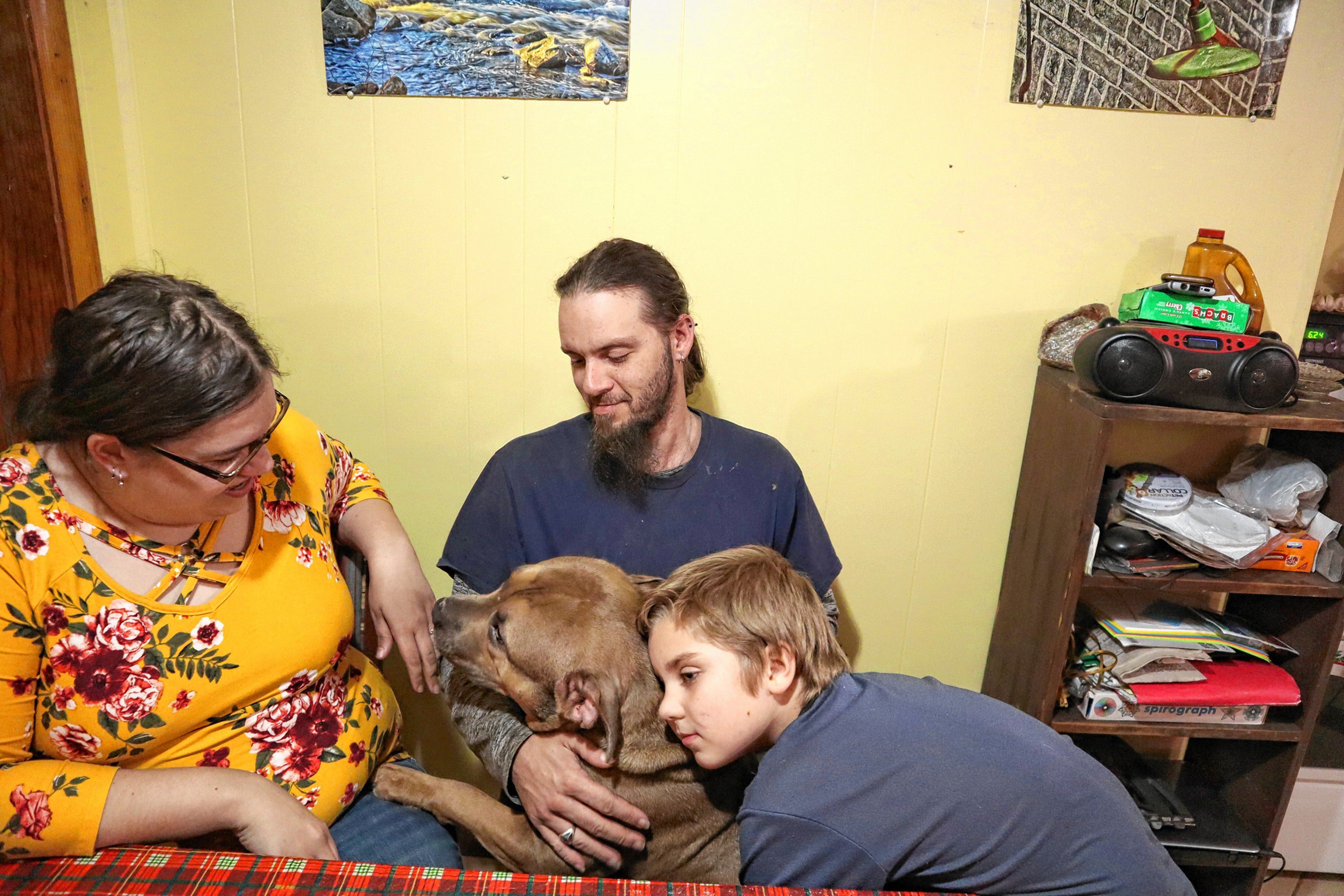 Shaye Campbell, 9, hugs his dog, Max, while playing around at his kitchen table with his father, Mark Aucoin, and his father’s girlfriend, Vicki Cobb. 