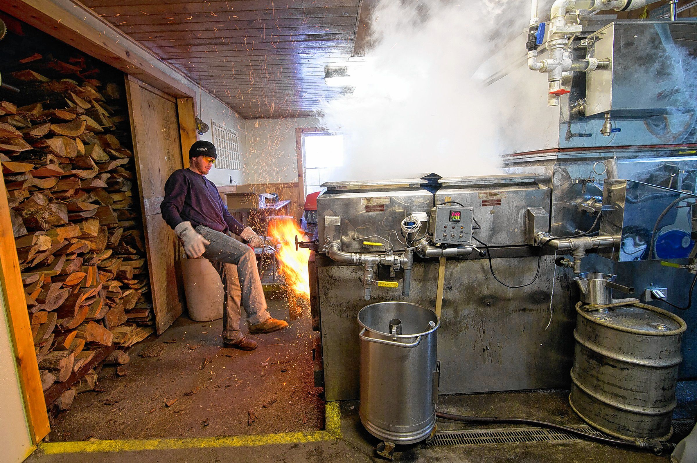 Jeff Moore of Windswept Maple Farm in Loudon uses his foot to close the door of the wood-fired evaporator at their maple processing building. It was warm enough this week to make syrup.  (GEOFF FORESTER / Monitor staff)  