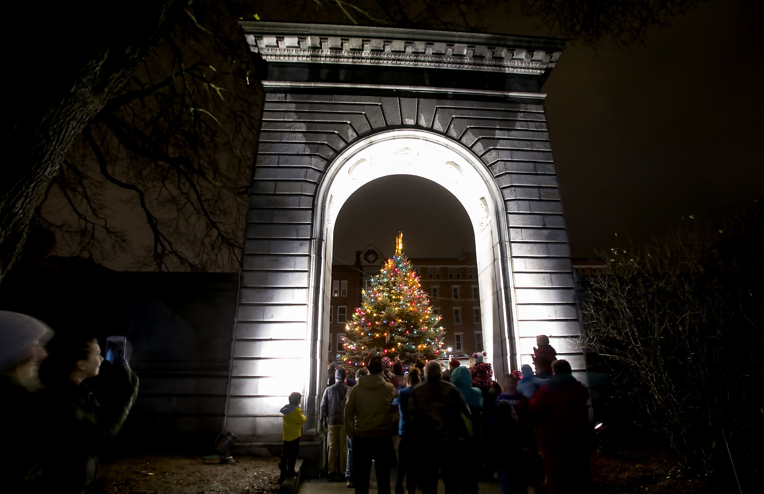 People watch from underneath the State House arch Friday night as the 30th annual Christmas tree lighting capped off a night of festivites. Santa Claus arrived via the Concord fire ladder truck and animal rides around the Park Street to Capitol Street and the evening finished with fireworks over Main Street. GEOFF FORESTER