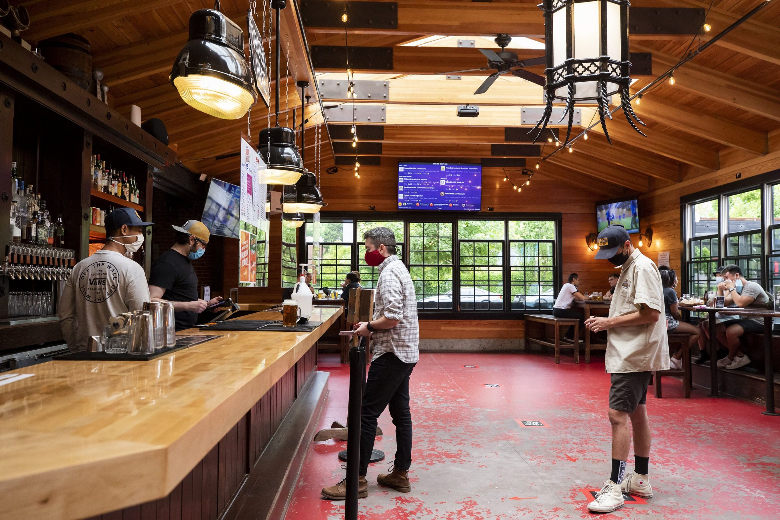 Brandon Owen and Charles McLean, right, line up to order at the bar at Rhein Haus Seattle on July 16, 2020. Both Owen, a server, and McLean, a sous chef, are not working at their respective local restaurants right now due to the pandemic. Safety measurements for COVID-19 seen at the bar include mandatory masks, industrial fans to increase airflow, social distancing while ordering and at tables, plexiglass dividers shielding bartenders, new contactless point-of-sale devices, and constant cleaning and disinfecting. (Bettina Hansen/Seattle Times/TNS) Bettina Hansen