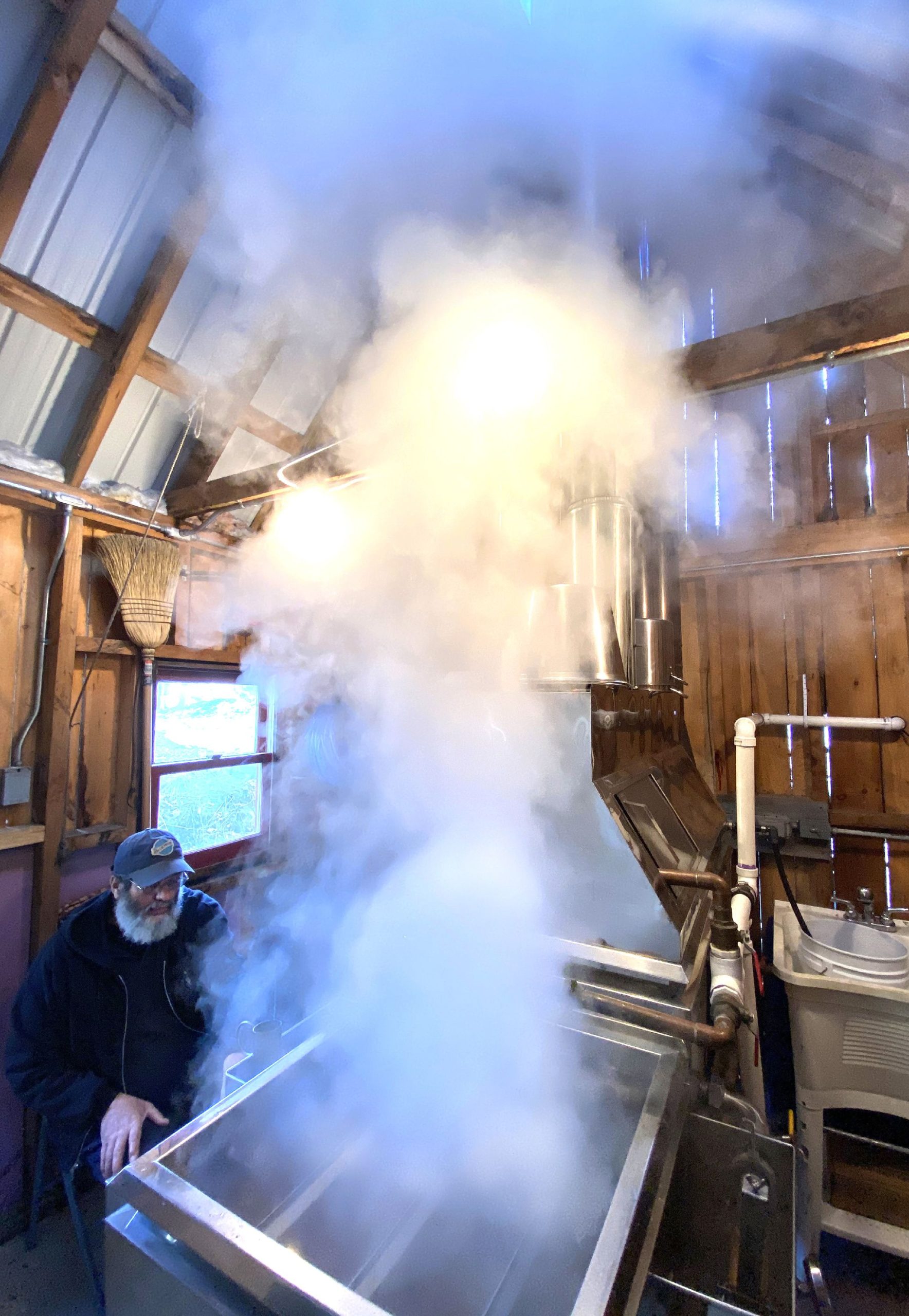 Russell Lampron of Red Roof Maples in Loudon looks at his hydrometer as the steam rises from  his evaporator as he boiled sap at his farm operation on Saturday, March 13,2021. Lampron is retiring after this maple season and moving to North Carolina. GEOFF FORESTER