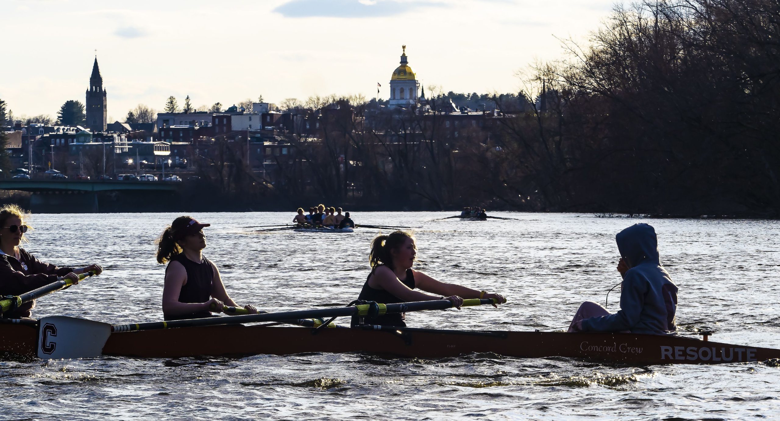 One of the two Concord girls crew boats make their way down the Merrimack River with the Concord skyline in the backround on Tuesday evening, April 5, 2022 on the first time on the water for the season. GEOFF FORESTER